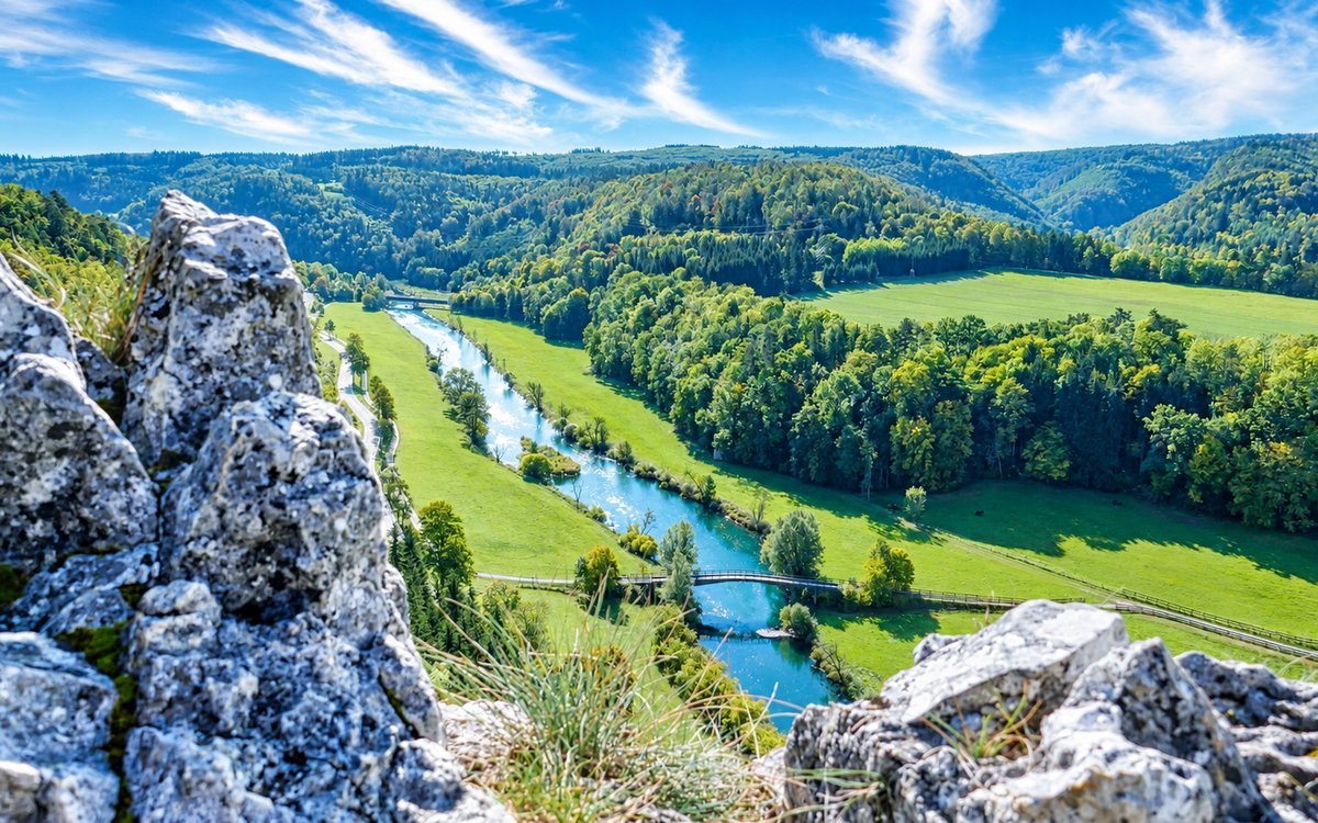 Blick von einem Felsen über das Donautal mit Fluss, Wiesen und bewaldeten Hängen